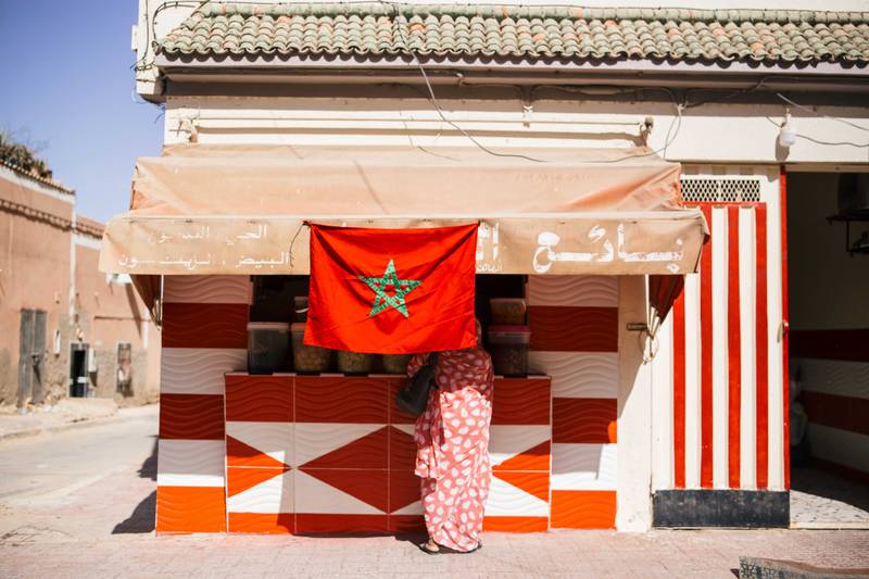 In Laayoune, a lady buys olives at a shop covered by the Moroccan flag.