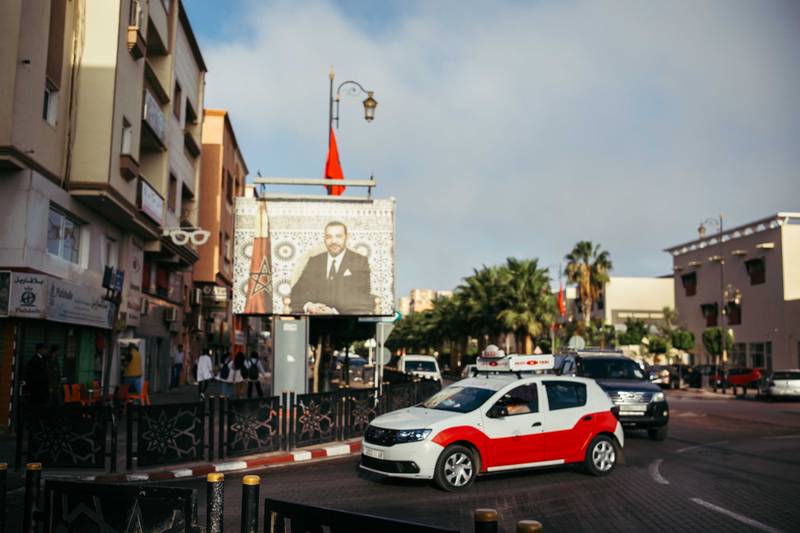 A taxi in Laayoune, Western Sahara’s unofficial capital, driving past a billboard reminding residents of Morocco’s rule.