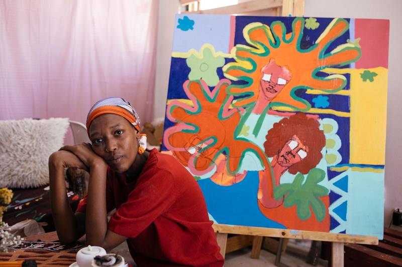 Yathrib Hassan in her home studio, in front of her latest painting in progress, which she says was inspired by memories of dancing in the rain with her sister outside their family home in Khartoum.